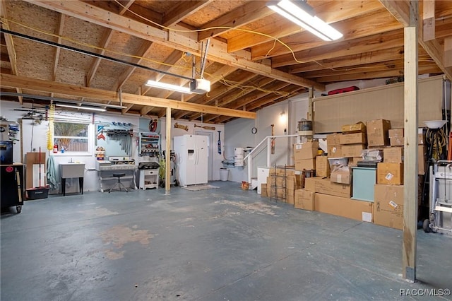 garage featuring a garage door opener, white fridge with ice dispenser, a workshop area, and sink