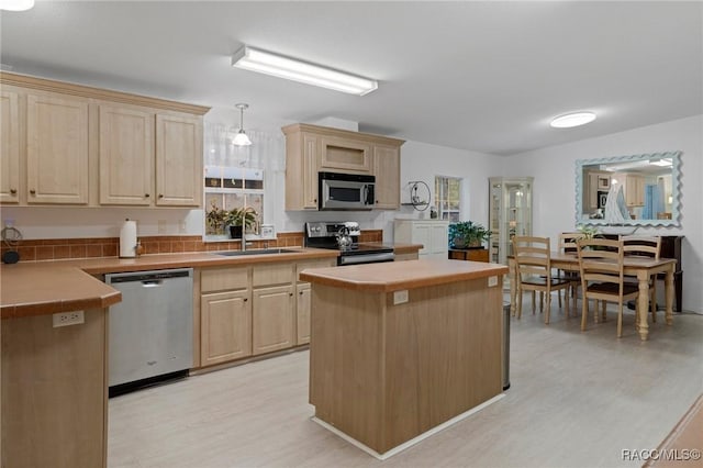 kitchen featuring stainless steel appliances, sink, decorative light fixtures, light brown cabinets, and a kitchen island