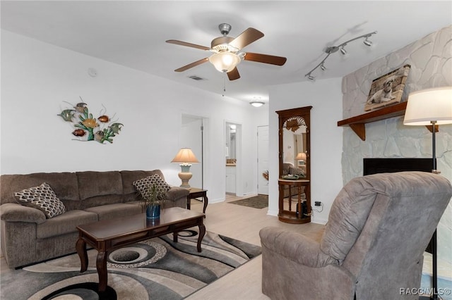 living room with track lighting, ceiling fan, and a stone fireplace