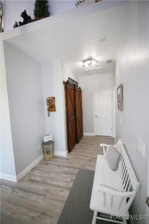 hallway with a barn door, visible vents, baseboards, and light wood-style floors