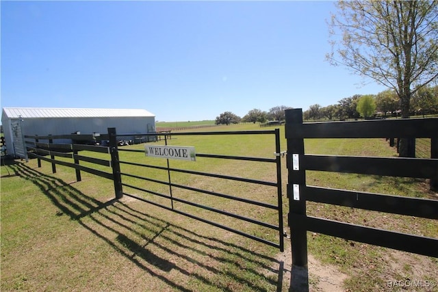 view of gate with a yard, a rural view, an outdoor structure, and fence