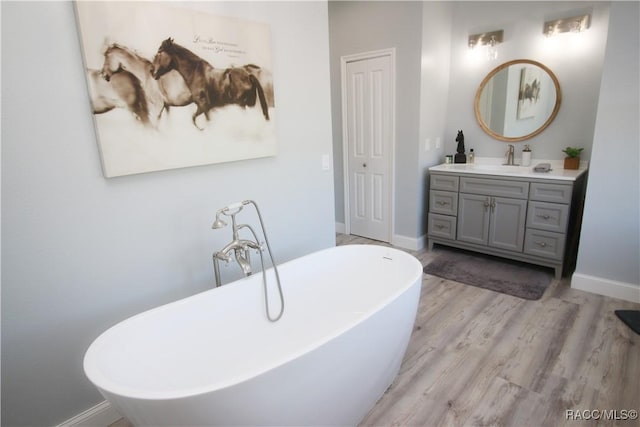 full bathroom featuring vanity, wood finished floors, baseboards, and a freestanding bath