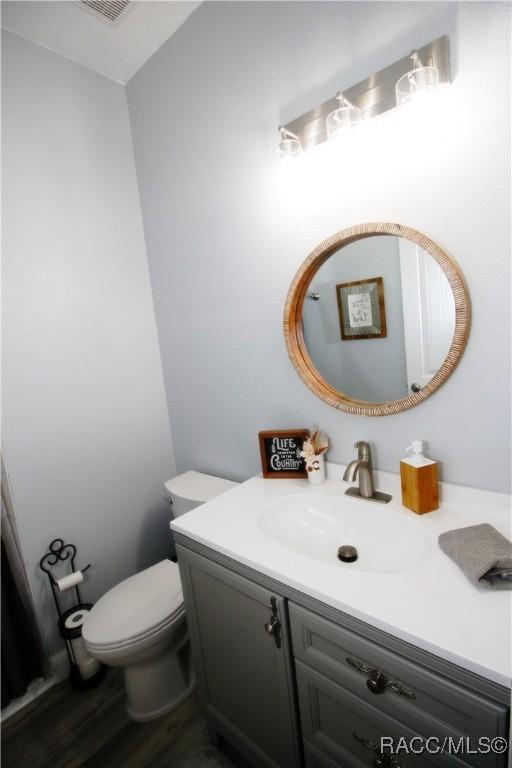 half bath featuring visible vents, toilet, wood finished floors, and vanity