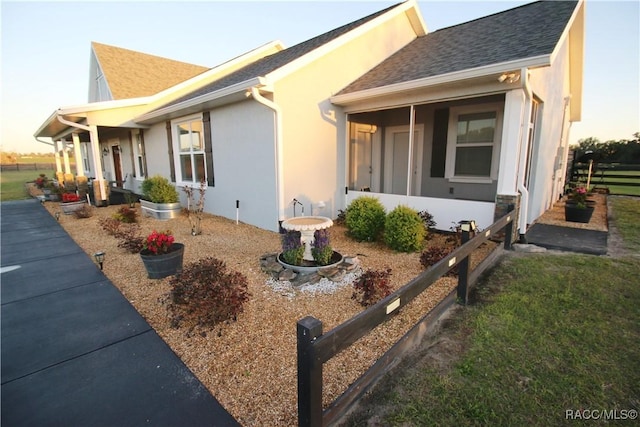 view of front of property featuring a shingled roof, a sunroom, and stucco siding