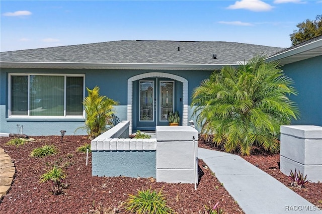 property entrance featuring french doors, stucco siding, and a shingled roof