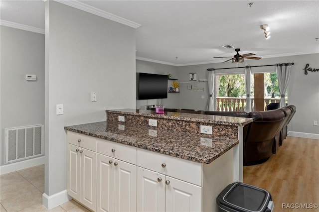 kitchen featuring white cabinetry, ceiling fan, ornamental molding, and dark stone countertops