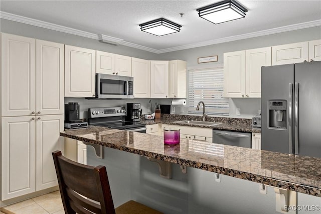 kitchen with sink, a breakfast bar area, dark stone countertops, white cabinetry, and stainless steel appliances