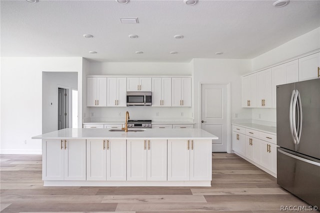 kitchen with appliances with stainless steel finishes, sink, white cabinetry, and an island with sink