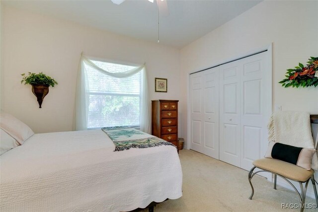 bedroom featuring light colored carpet, ceiling fan, and a closet