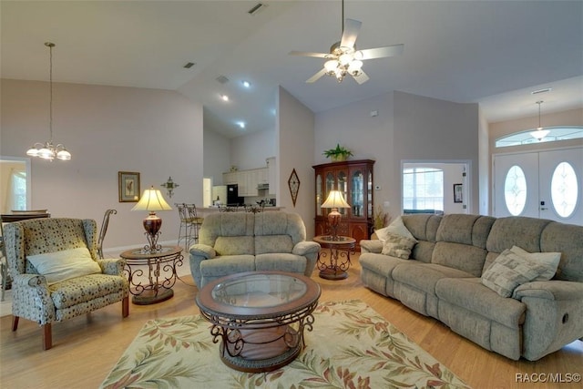 living room with high vaulted ceiling, ceiling fan with notable chandelier, and light wood-type flooring