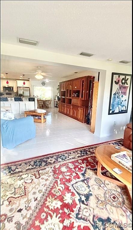 living room featuring a textured ceiling, ceiling fan, and light tile patterned floors