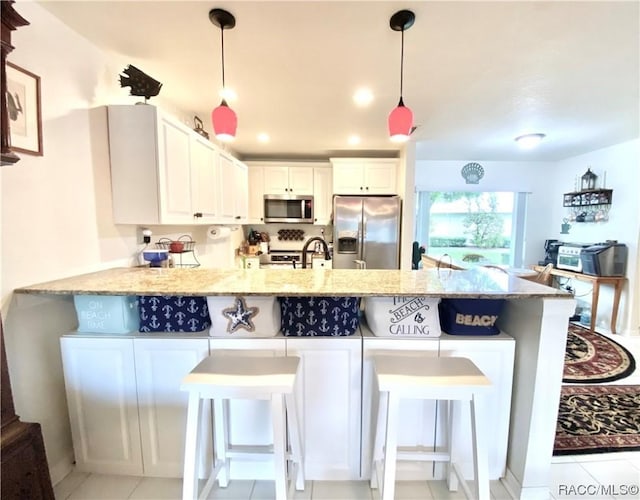 kitchen with hanging light fixtures, white cabinets, kitchen peninsula, and appliances with stainless steel finishes