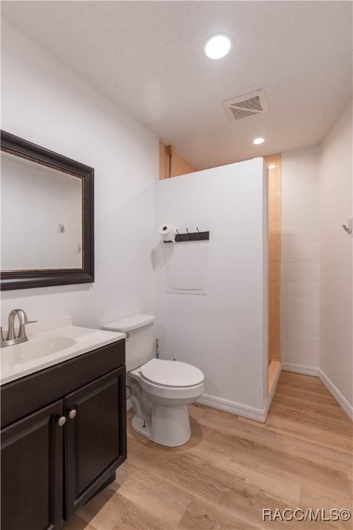 bathroom with tiled shower, hardwood / wood-style floors, vanity, and toilet