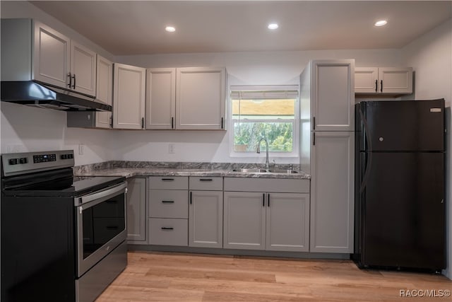 kitchen with black fridge, sink, stainless steel electric range oven, light wood-type flooring, and light stone counters