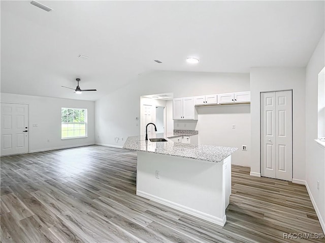 kitchen featuring sink, white cabinetry, light stone counters, hardwood / wood-style flooring, and a kitchen island with sink