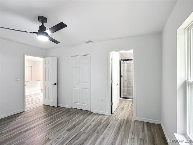 unfurnished bedroom featuring ceiling fan, ensuite bathroom, light hardwood / wood-style floors, and a closet