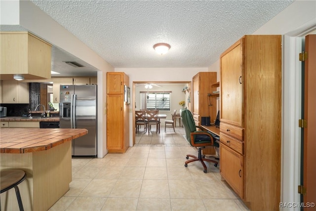 kitchen with a textured ceiling, visible vents, light tile patterned flooring, tile countertops, and stainless steel fridge with ice dispenser