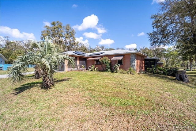 ranch-style home with metal roof, roof mounted solar panels, a front yard, and a sunroom