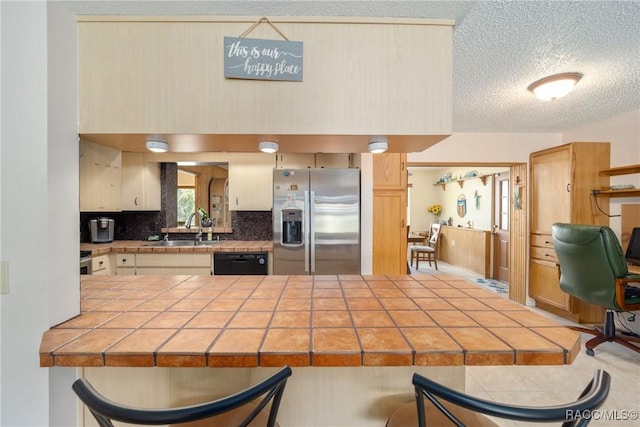 kitchen with a sink, tile counters, a breakfast bar, dishwasher, and stainless steel fridge
