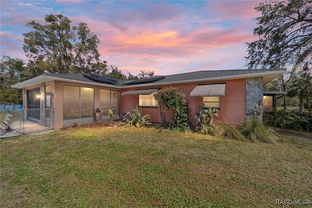 view of front of property featuring metal roof, solar panels, stucco siding, a front lawn, and a sunroom