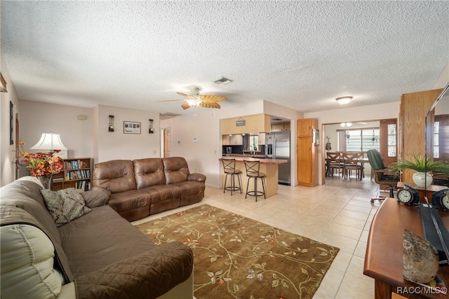 living area featuring light tile patterned floors, a textured ceiling, visible vents, and a ceiling fan