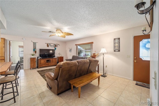 living area featuring baseboards, light tile patterned floors, ceiling fan, and a textured ceiling