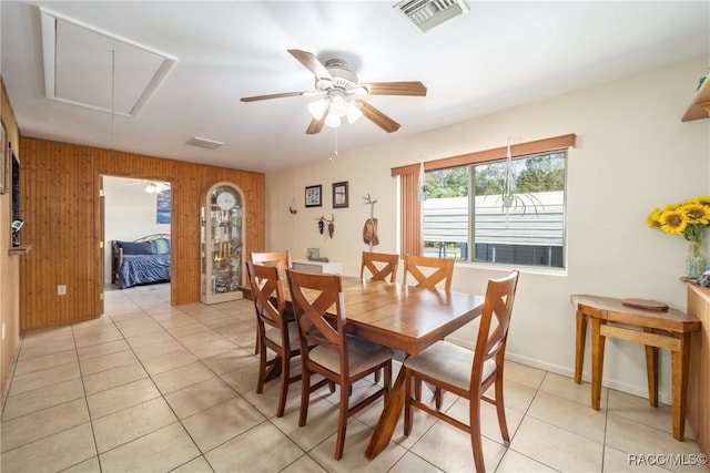 dining room featuring light tile patterned floors, attic access, visible vents, a ceiling fan, and wooden walls