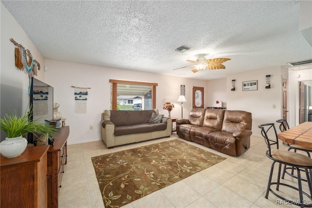 living room featuring light tile patterned floors, visible vents, a ceiling fan, and a textured ceiling