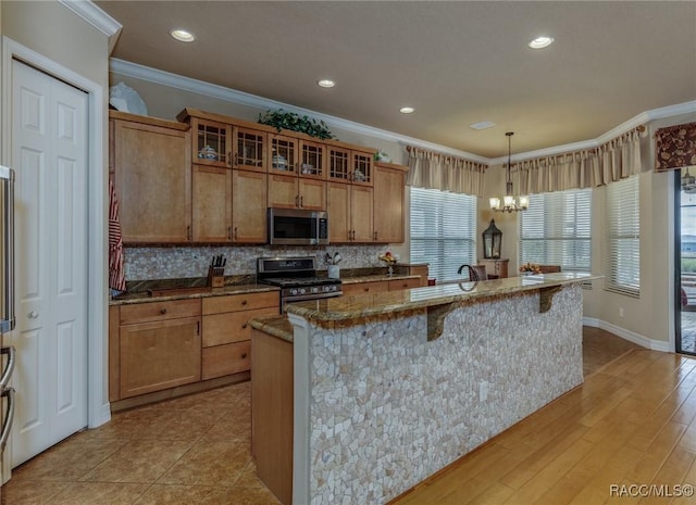 kitchen with stainless steel appliances, glass insert cabinets, hanging light fixtures, and an island with sink