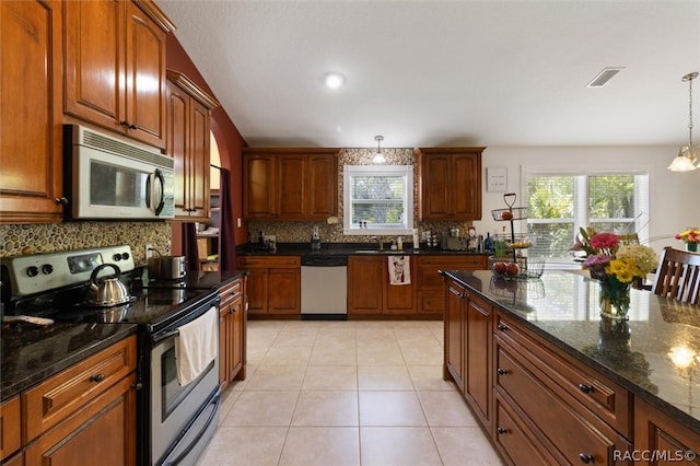 kitchen featuring a wealth of natural light, dark stone countertops, hanging light fixtures, and appliances with stainless steel finishes