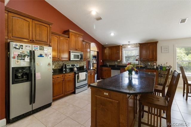 kitchen with light tile patterned floors, vaulted ceiling, decorative backsplash, a kitchen island, and appliances with stainless steel finishes