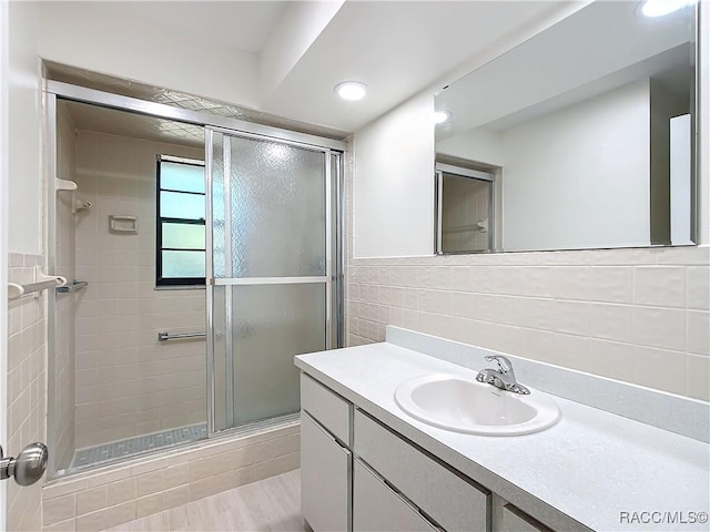 bathroom with tasteful backsplash, a shower with door, vanity, and tile walls