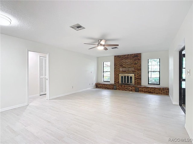 unfurnished living room featuring ceiling fan, a fireplace, a healthy amount of sunlight, and a textured ceiling