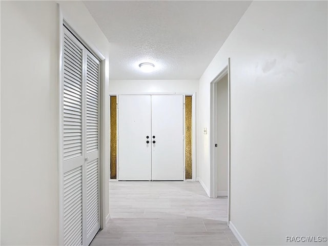 hall featuring light wood-type flooring and a textured ceiling