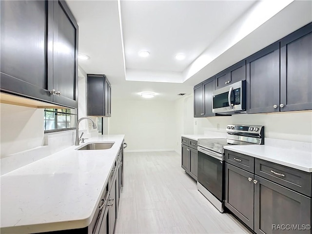 kitchen featuring light stone countertops, appliances with stainless steel finishes, a tray ceiling, and sink