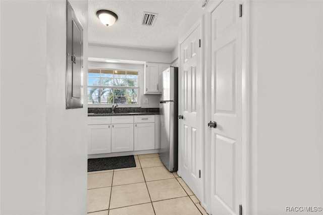 kitchen with stainless steel refrigerator, sink, light tile patterned floors, and white cabinets