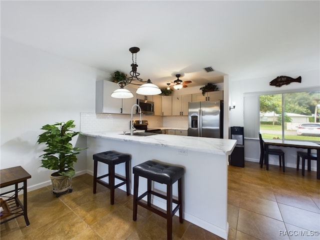 kitchen featuring sink, appliances with stainless steel finishes, hanging light fixtures, backsplash, and kitchen peninsula