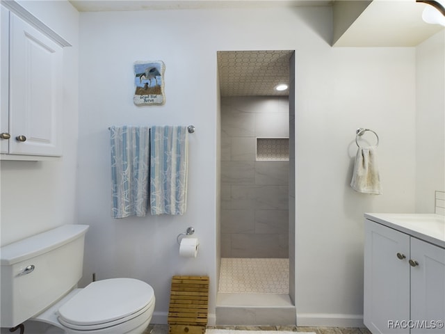 bathroom featuring a tile shower, vanity, and toilet