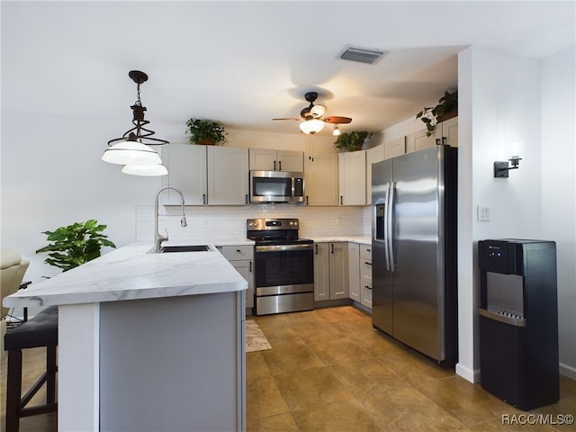 kitchen featuring gray cabinets, a breakfast bar, appliances with stainless steel finishes, hanging light fixtures, and kitchen peninsula