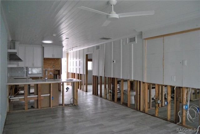 kitchen featuring ceiling fan, wood-type flooring, wall chimney range hood, white cabinets, and sink