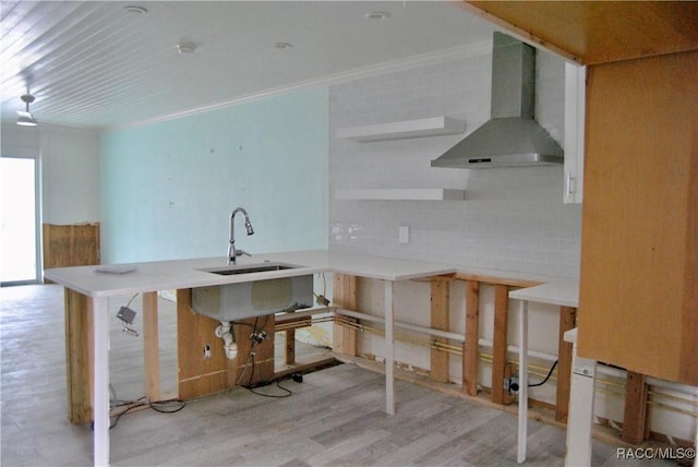 kitchen with kitchen peninsula, decorative backsplash, light wood-type flooring, wall chimney exhaust hood, and sink