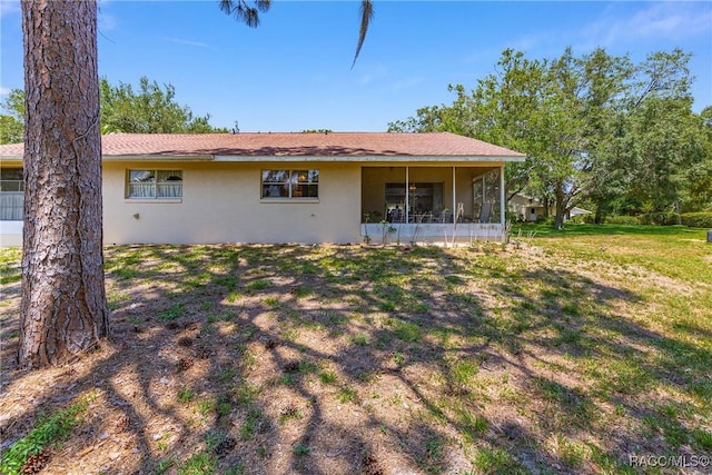 back of house featuring a yard, stucco siding, and a sunroom