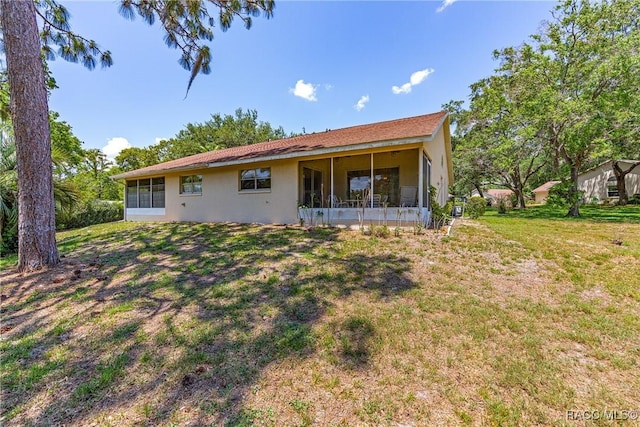 rear view of house with a yard, a sunroom, and stucco siding