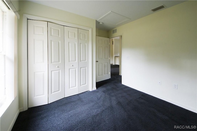 unfurnished bedroom with multiple windows, dark colored carpet, and a closet