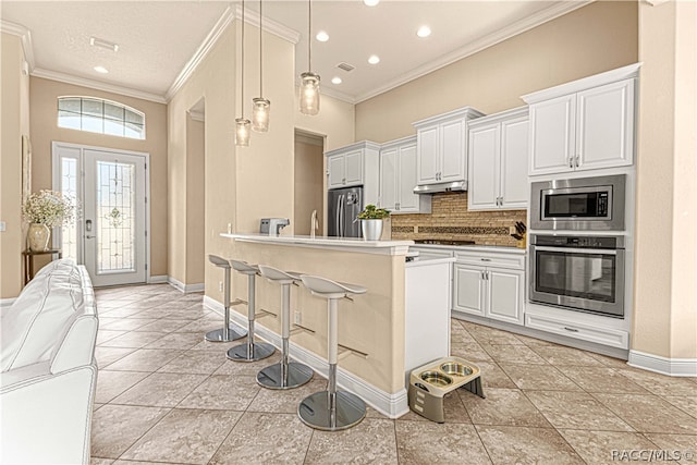 kitchen with white cabinets, hanging light fixtures, decorative backsplash, ornamental molding, and stainless steel appliances