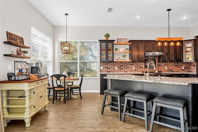 kitchen with dark brown cabinetry, a breakfast bar, decorative light fixtures, and light wood-type flooring