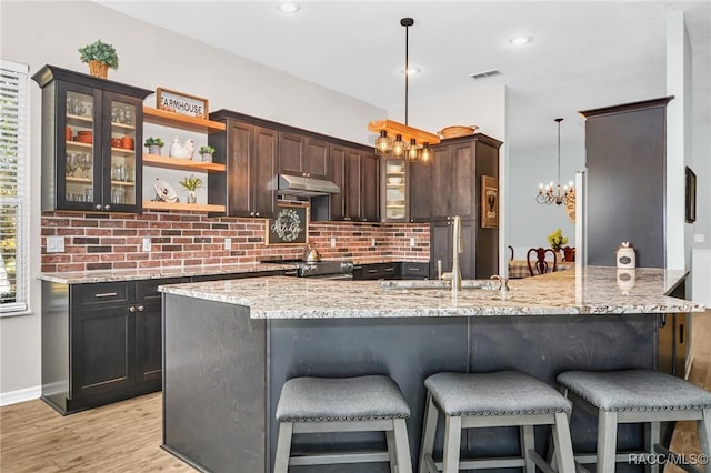 kitchen with sink, hanging light fixtures, kitchen peninsula, dark brown cabinets, and light wood-type flooring