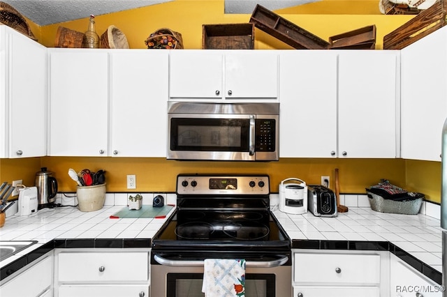 kitchen featuring white cabinetry, appliances with stainless steel finishes, sink, and tile countertops