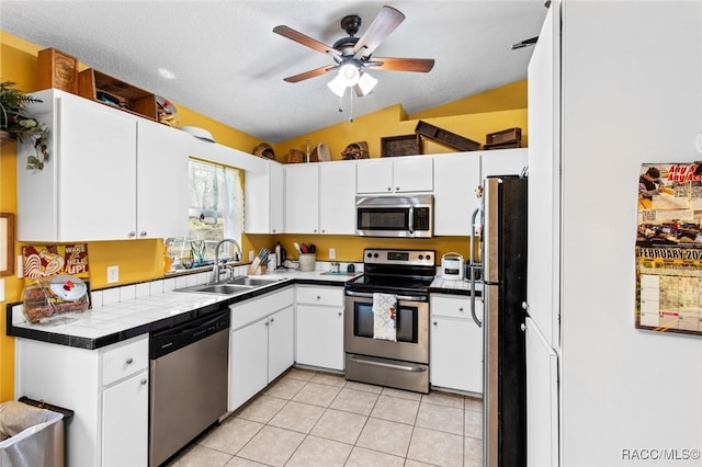 kitchen with sink, tile countertops, white cabinets, and appliances with stainless steel finishes