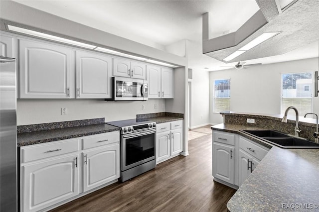 kitchen featuring a ceiling fan, dark countertops, a sink, dark wood-style floors, and stainless steel appliances